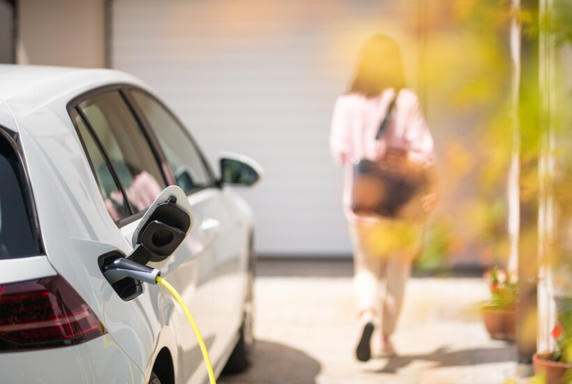 Shelly PRO 3EM 400A – ładowanie samochodu elektrycznego. Wtyczka doładowania w gniazdku, żółty kabel, kobieta w tle.