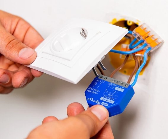 Shelly 1 Gen4 – biały przełącznik w ścianie, moduł Shelly Good 12V-24V podczas instalacji.