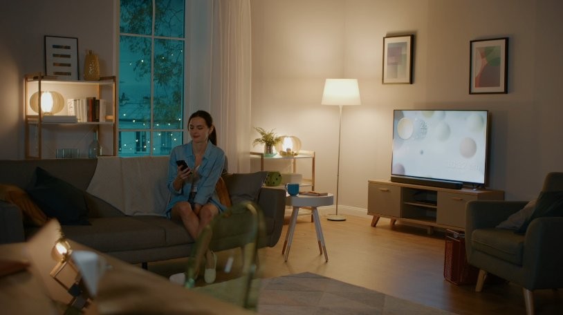 Shelly 2PM Gen3 - Sterowanie smart home z aplikacji Shelly 2PM Gen3 – inteligentny dom: kobieta steruje oświetleniem i urządzeniami przez aplikację w komfortowym salonie.