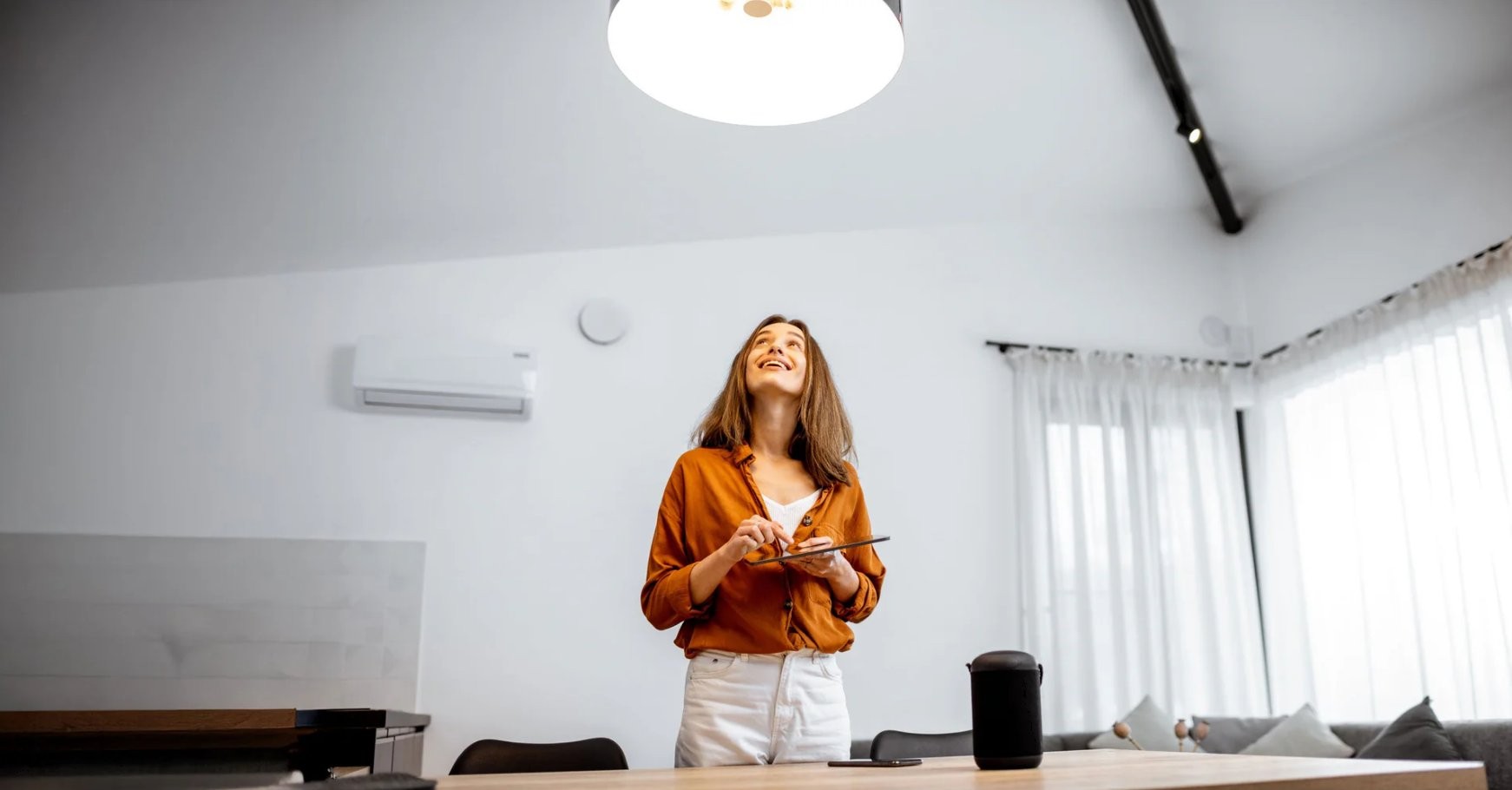 Shelly 1L Gen3 WiFi – inteligentne sterowanie w domu Shelly 1L Gen3 WiFi - inteligentny dom: kobieta z tabletem w nowoczesnym wnętrzu, klimatyzator i sterowniki na ścianie.