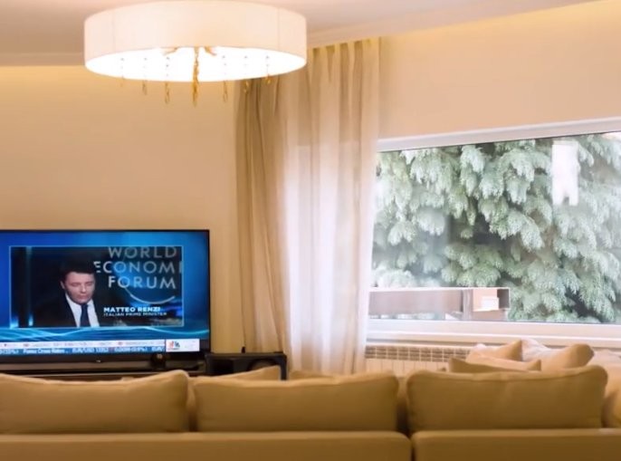 Domowy salon z telewizorem Salon z beżowym sofa i dużym telewizorem w tle, wyświetlającym program World Economic Forum