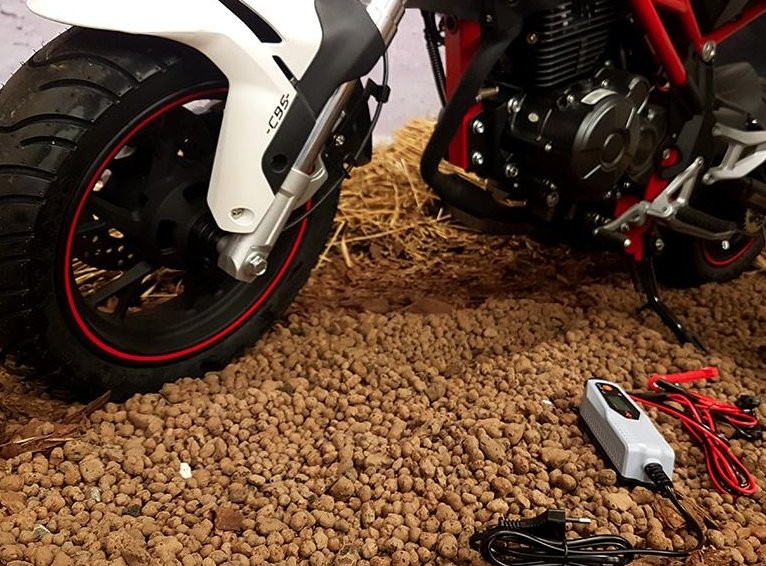 Ładowarka do motocykla C-95 Ładowarka do akumulatorów 12V, biało-czerwony motocykl na tle kamieni